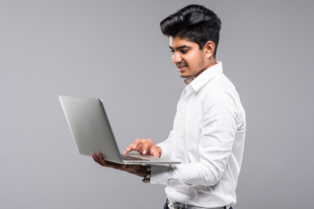 Young indian man with laptop on gray wall