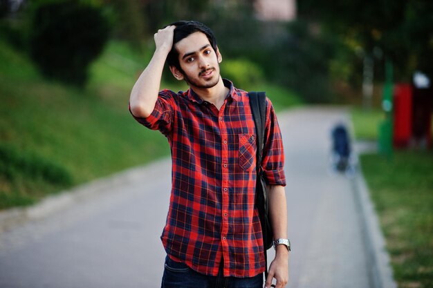 Young indian student man at red checkered shirt and jeans with backpack posed at street
