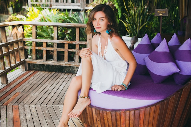 Free photo young innocent pure beautiful woman dreaming, sitting at couch in white dress, romantic, lyrical, thinking, green tropical nature, summer, relaxed, chilling, legs, resort hotel