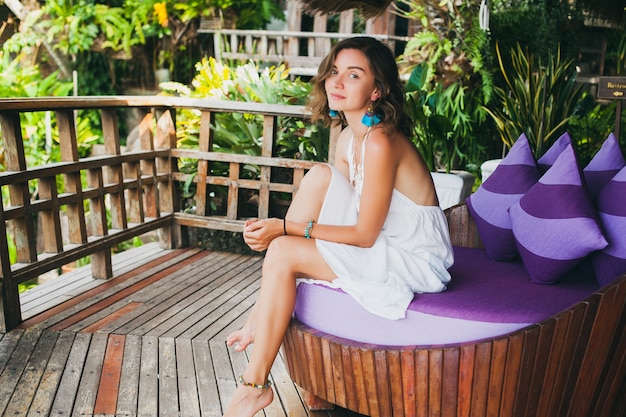 Young innocent pure beautiful woman dreaming, sitting at couch in white dress, romantic, lyrical, thinking, green tropical nature, summer, relaxed, chilling, legs, resort hotel