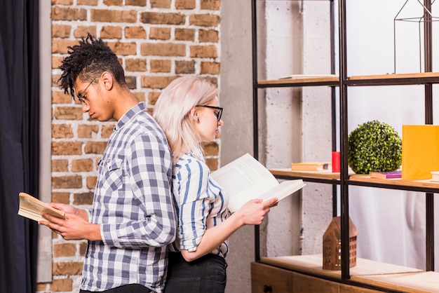 Free photo young interracial young couple standing back to back reading the book