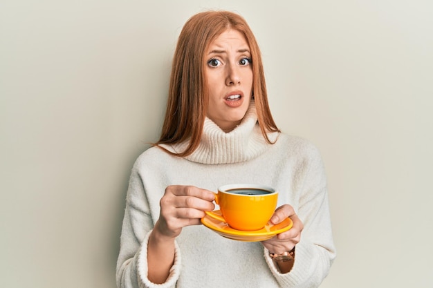 Foto gratuita giovane donna irlandese che beve una tazza di caffè concetto di dubbio di espressione all'oscuro e confuso