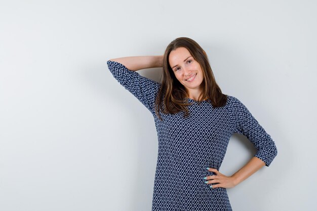 The young is smiling by placing her right hand behind head and other on waist on white background