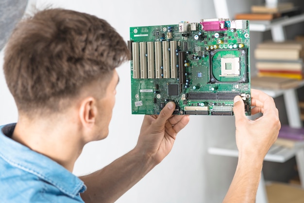 Young IT technician looking at motherboard