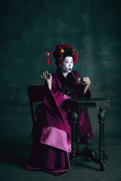 Young japanese woman as geisha on dark green. Retro style, comparison of eras concept.