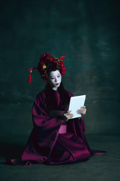 Young japanese woman as geisha on dark green. Retro style, comparison of eras concept.