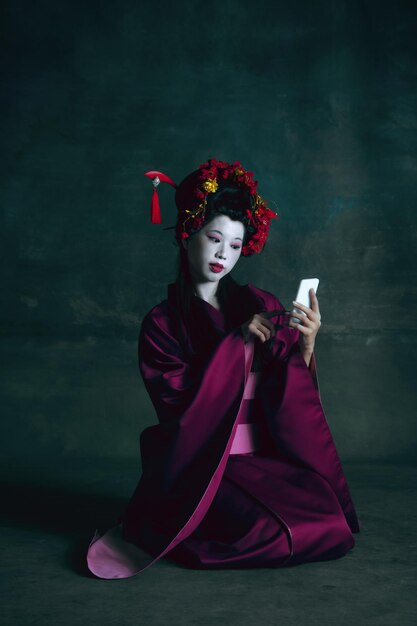 Young japanese woman as geisha on dark green. Retro style, comparison of eras concept.