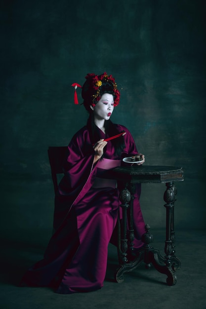 Foto gratuita giovane donna giapponese come geisha sul muro verde scuro
