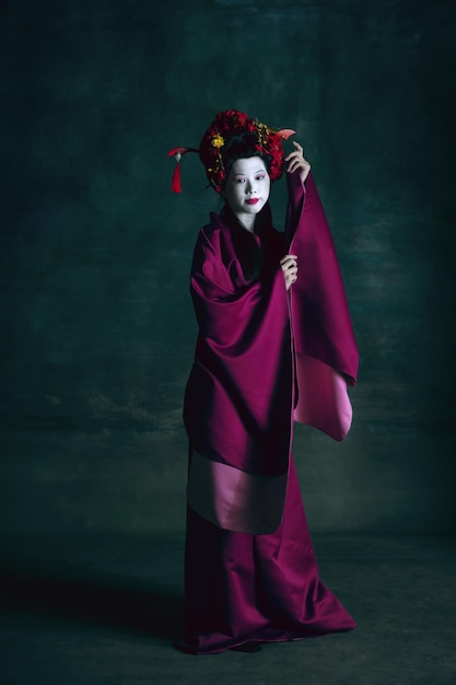 Free photo young japanese woman as geisha on dark green