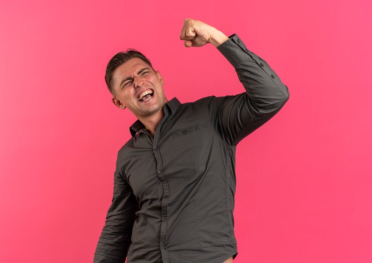 Free Photo young joyful blonde handsome man holds fist up isolated on pink background with copy space