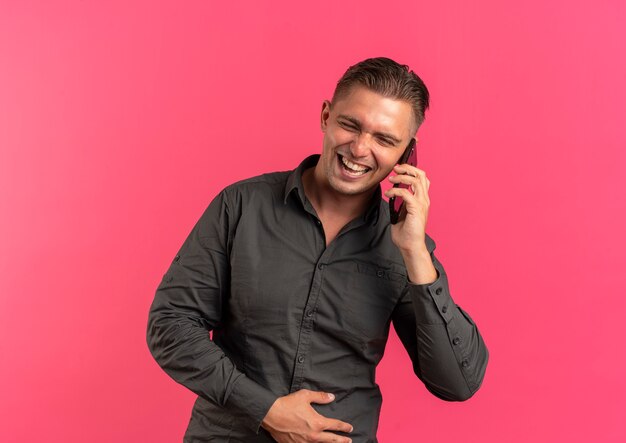 Young joyful blonde handsome man talks on phone isolated on pink space with copy space