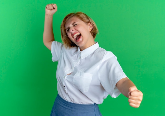 young joyful blonde russian girl holds fist up and out isolated on green background with copy space