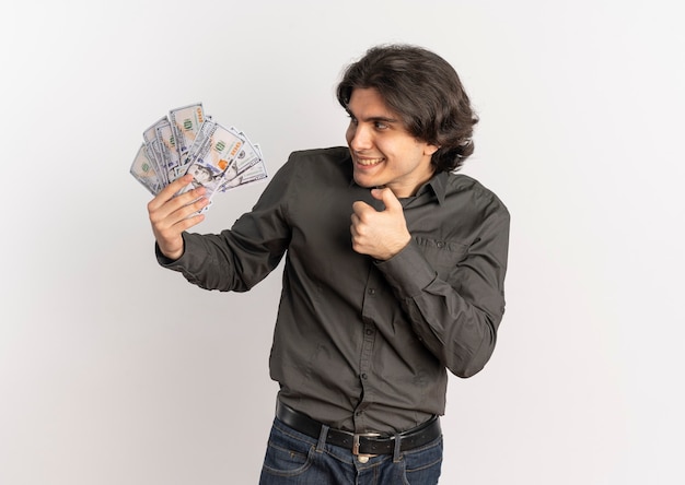 Молодой радостный красивый кавказский мужчина держит и смотрит на деньги, изолированные на белом фоне с копией пространства