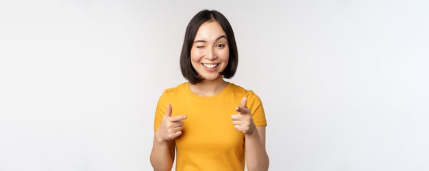 Молодая корейская студентка показывает пальцем на камеру и улыбается, поздравляя вас с выбором приглашения