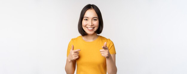 Молодая корейская студентка показывает пальцем на камеру и улыбается, поздравляя вас с выбором приглашения