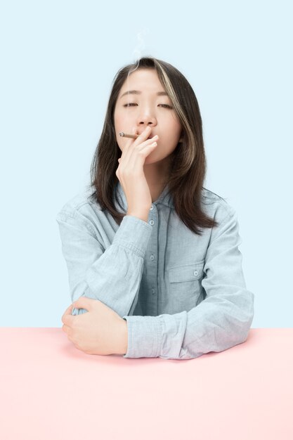 Young korean women smoking cigar while sitting at table at studio. Trendy colors