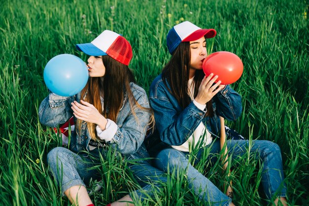 Young ladies blowing colored balloons on green grass