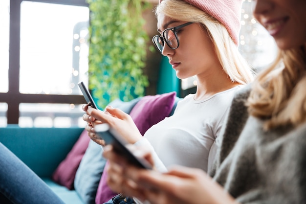 Young ladies sitting in cafe and using mobile phones.