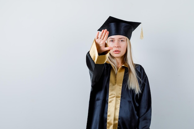 Молодая дама в академической одежде показывает жест стоп и выглядит встревоженной