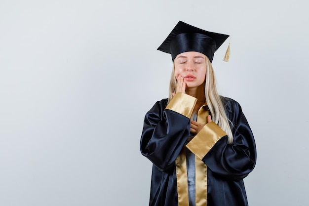 Foto gratuita giovane donna in abiti accademici che soffre di mal di denti e sembra indisposta