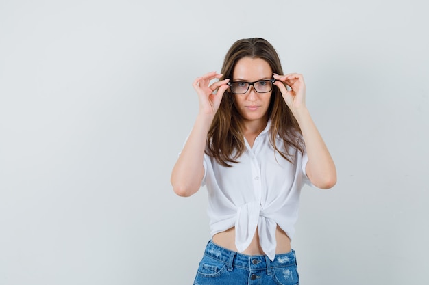 Young lady adjusting her glasses in white blouse,glasses , front view.