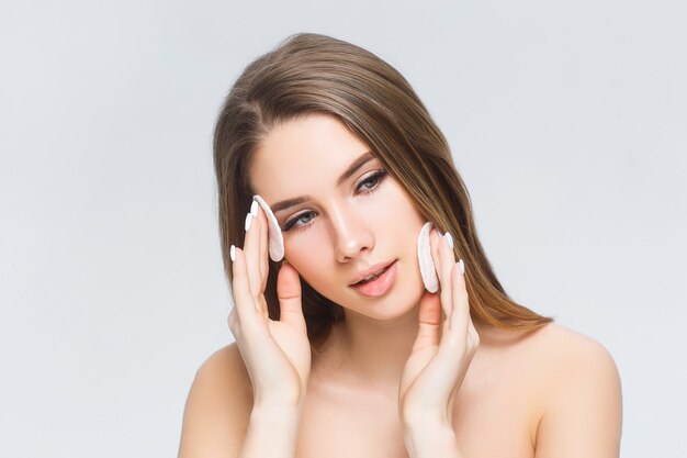 Young lady applying powdered foundation on her face with cosmetic sponge puff