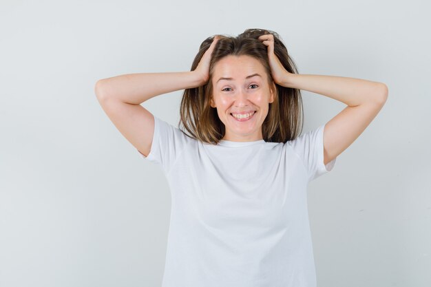 Young lady arranging hair with hands in white t-shirt and looking alluring 