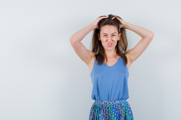 Young lady arranging her hair in singlet, skirt and looking alluring