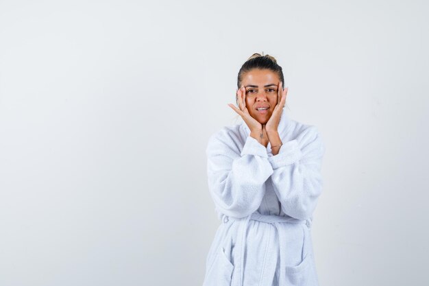 Young lady in bathrobe holding hands on cheeks and looking cute