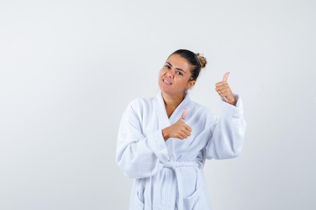 Young lady in bathrobe showing thumbs up and looking joyful
