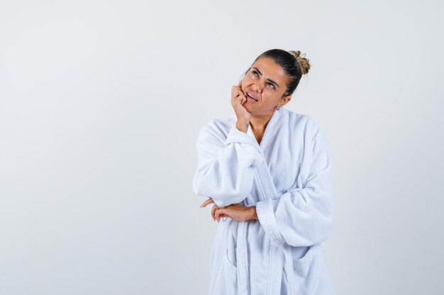 Young lady in bathrobe standing in thinking pose and looking thoughtful