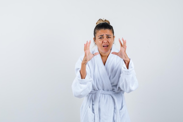 Young lady in bathrobe stretching hand in questioning gesture and looking confused