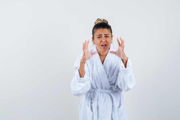 Young lady in bathrobe stretching hand in questioning gesture and looking confused