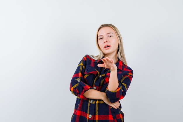 Young lady beckoning someone forward in checked shirt and looking confident , front view.