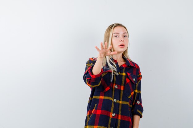 Young lady beckoning someone forward in checked shirt and looking confident , front view.