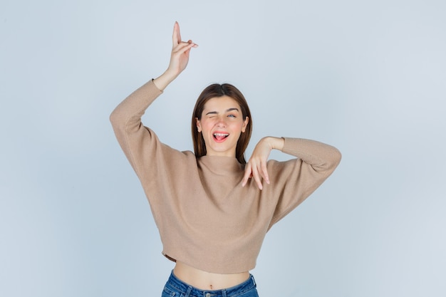 Young lady in beige sweater, jeans pointing up and down and looking cheery , front view.