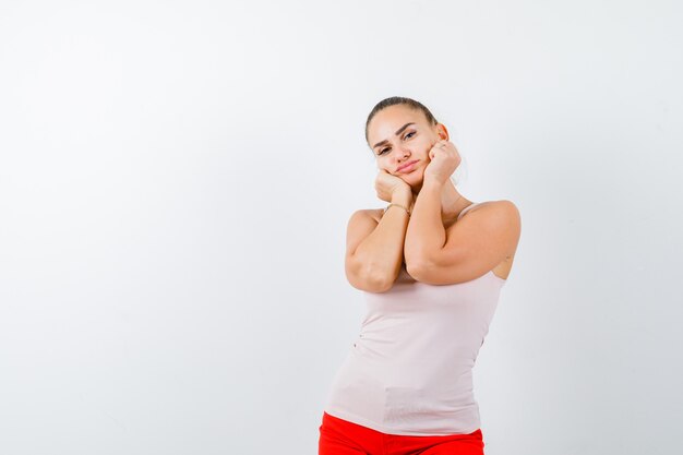 Young lady in beige tank top pillowing face on her hands and looking pensive