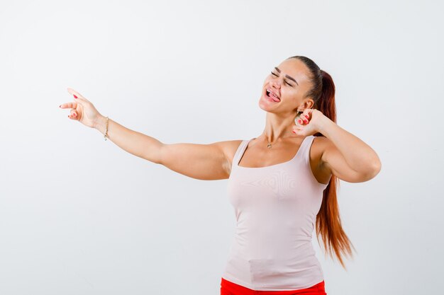 Young lady in beige tank top pointing aside and looking happy , front view.