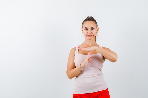 Young lady in beige tank top showing time break gesture and looking confident