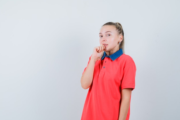 Young lady biting finger in t-shirt and looking embarrassed. front view.