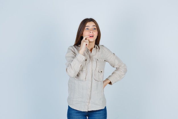 Young lady biting her finger in casual, jeans and looking astonished , front view.