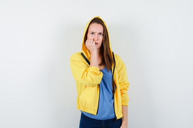 Young lady biting her nails in t-shirt, jacket and looking gloomy