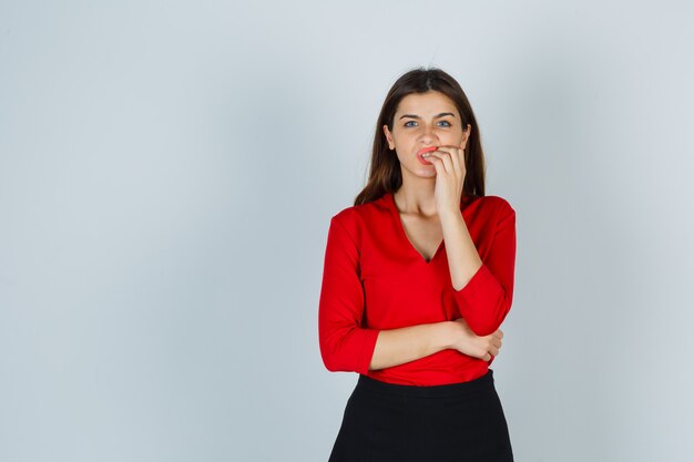 Young lady biting nails in red blouse, skirt and looking stressed