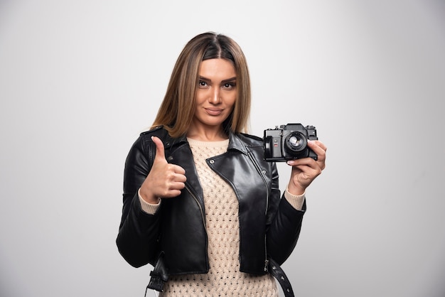 Young lady in black leather jacket taking photos with camera in a positive and smiling manner.