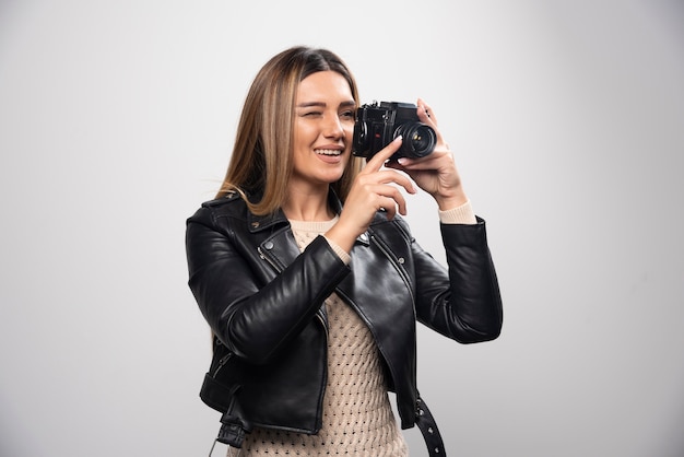 Young lady in black leather jacket taking photos with camera in a positive and smiling manner.