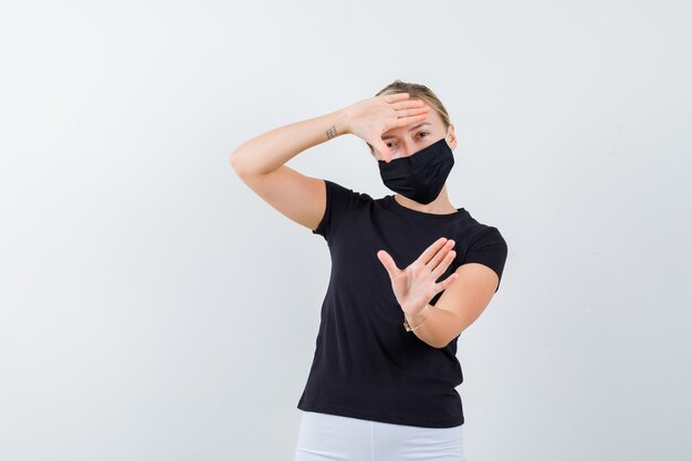 Young lady in black t-shirt, mask making frame gesture and looking cheery , front view.