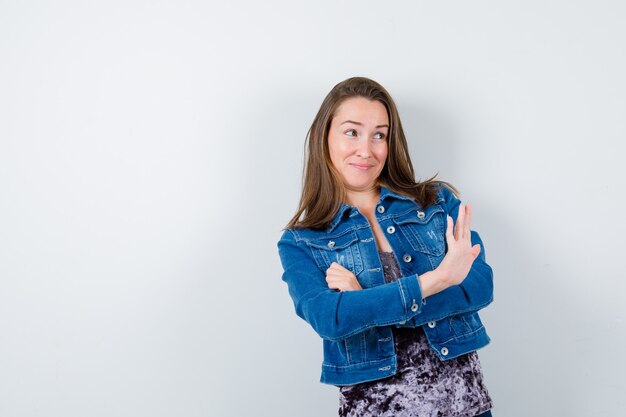 Young lady in blouse, denim jacket showing stop gesture and looking confident , front view.