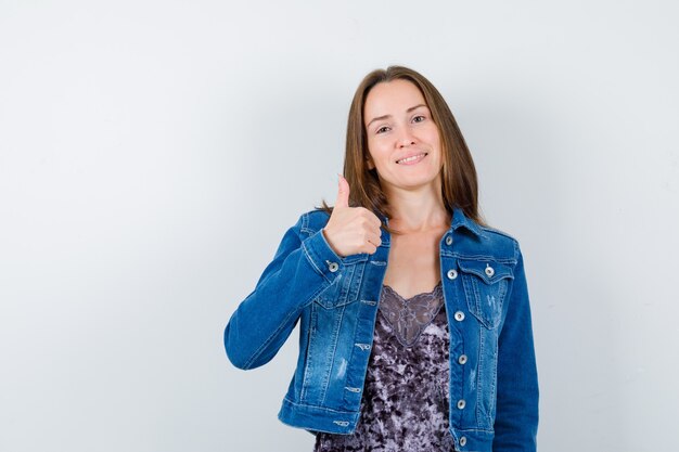 Free photo young lady in blouse, denim jacket showing thumb up and looking glad , front view.