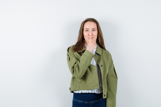 Young lady in blouse holding finger on nose and looking nice , front view.