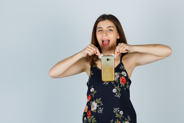 Young lady in blouse holding smartphone and looking happy , front view.